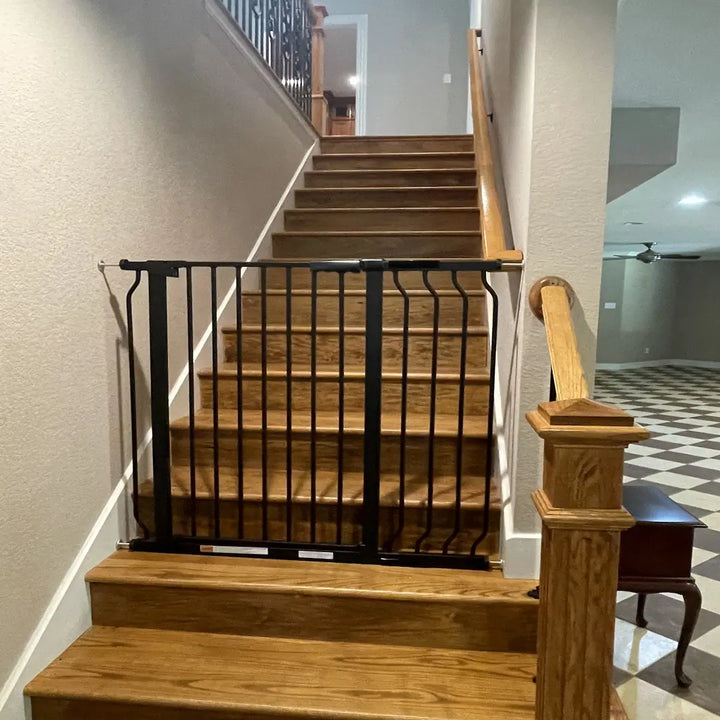 FairyBaby W282 black safety baby gate installed at the bottom of a modern hallway staircase