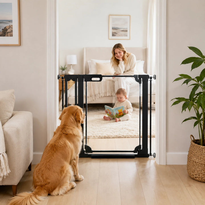 A black metal pet gate with safety panels stands in a doorway of a bright, modern living room. A golden retriever sits attentively on the left, while a woman and a young child are visible behind the gate in a softly lit nursery or playroom.